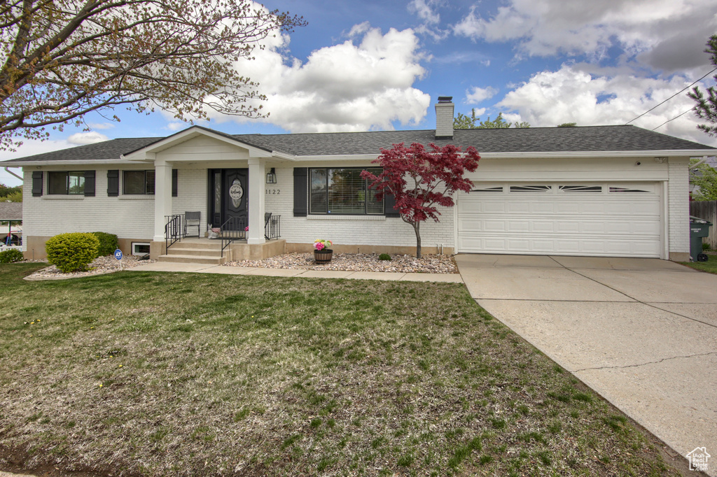 Single story home with a garage, a front lawn, a chimney, brick siding, and driveway