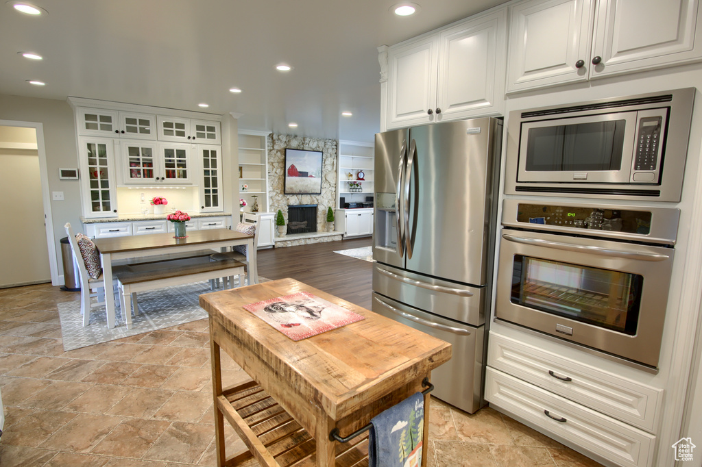 Kitchen with stainless steel appliances, white cabinetry, stone finish flooring, recessed lighting, and glass insert cabinets