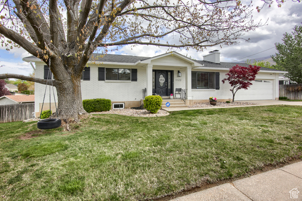 Ranch-style house with fence, an attached garage, brick siding, a front yard, and a chimney