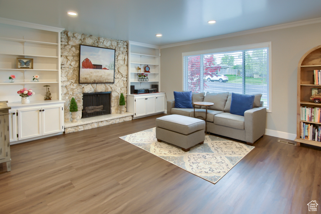 Living room with crown molding, baseboards, a stone fireplace, and wood finished floors