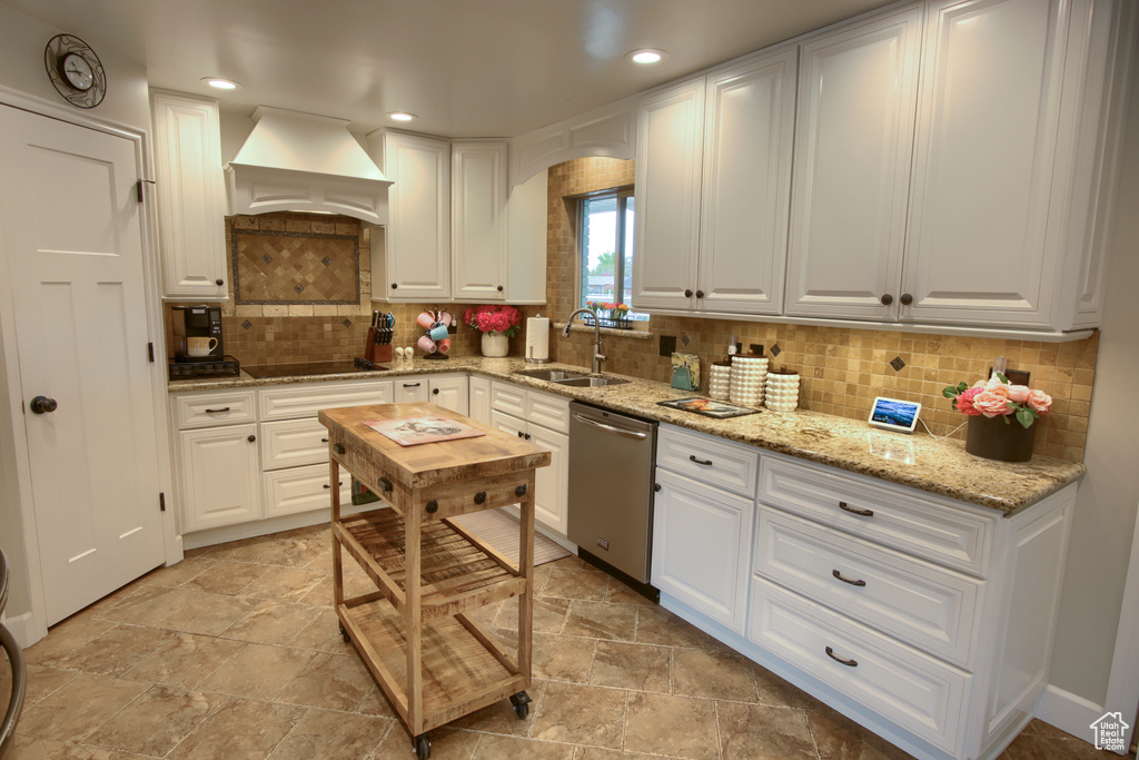 Kitchen with stainless steel dishwasher, premium range hood, white cabinetry, a sink, and stone finish flooring