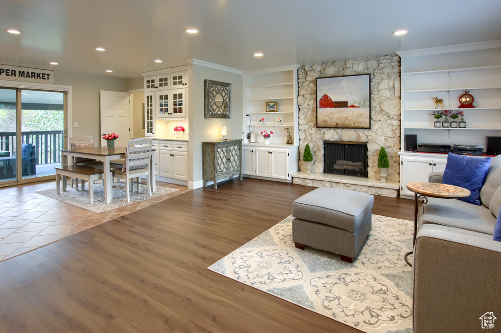 Living room with dark wood finished floors, a stone fireplace, built in features, recessed lighting, and ornamental molding