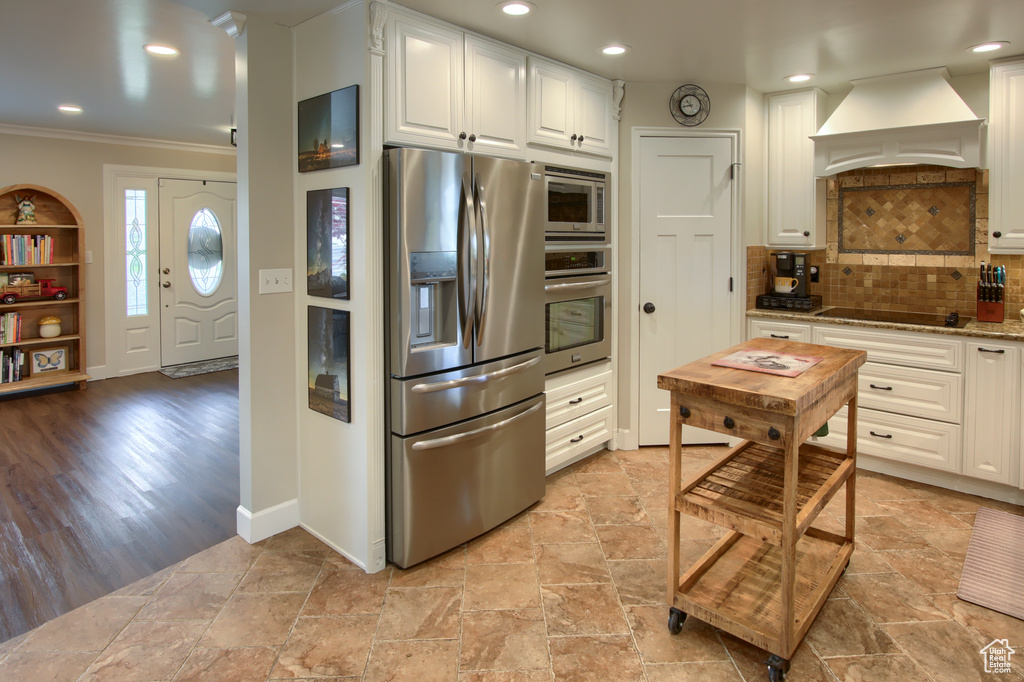Kitchen featuring white cabinets, appliances with stainless steel finishes, custom exhaust hood, and ornamental molding