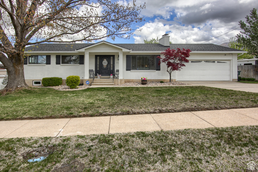 Single story home with a garage, a front lawn, a chimney, brick siding, and concrete driveway