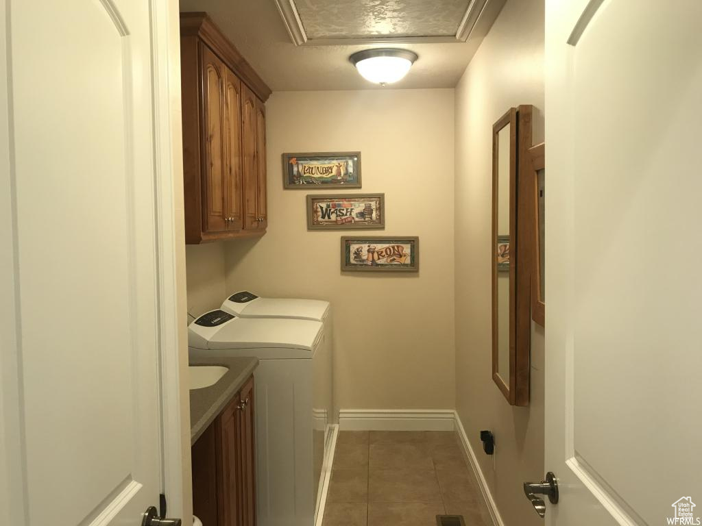 Clothes washing area with baseboards, cabinet space, light tile patterned floors, and washing machine and dryer