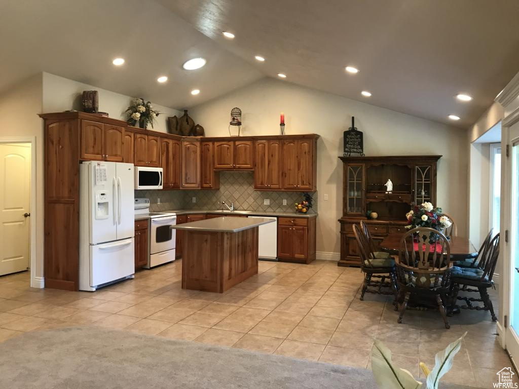 Kitchen featuring a kitchen island, tasteful backsplash, vaulted ceiling, light tile patterned floors, and white appliances