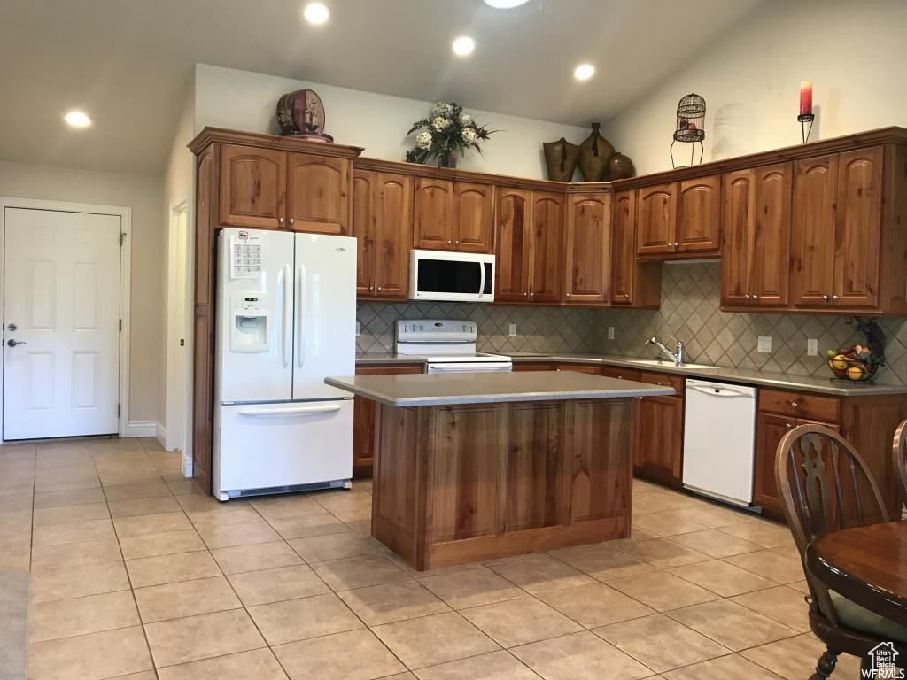 Kitchen with lofted ceiling, a kitchen island, white appliances, and tasteful backsplash
