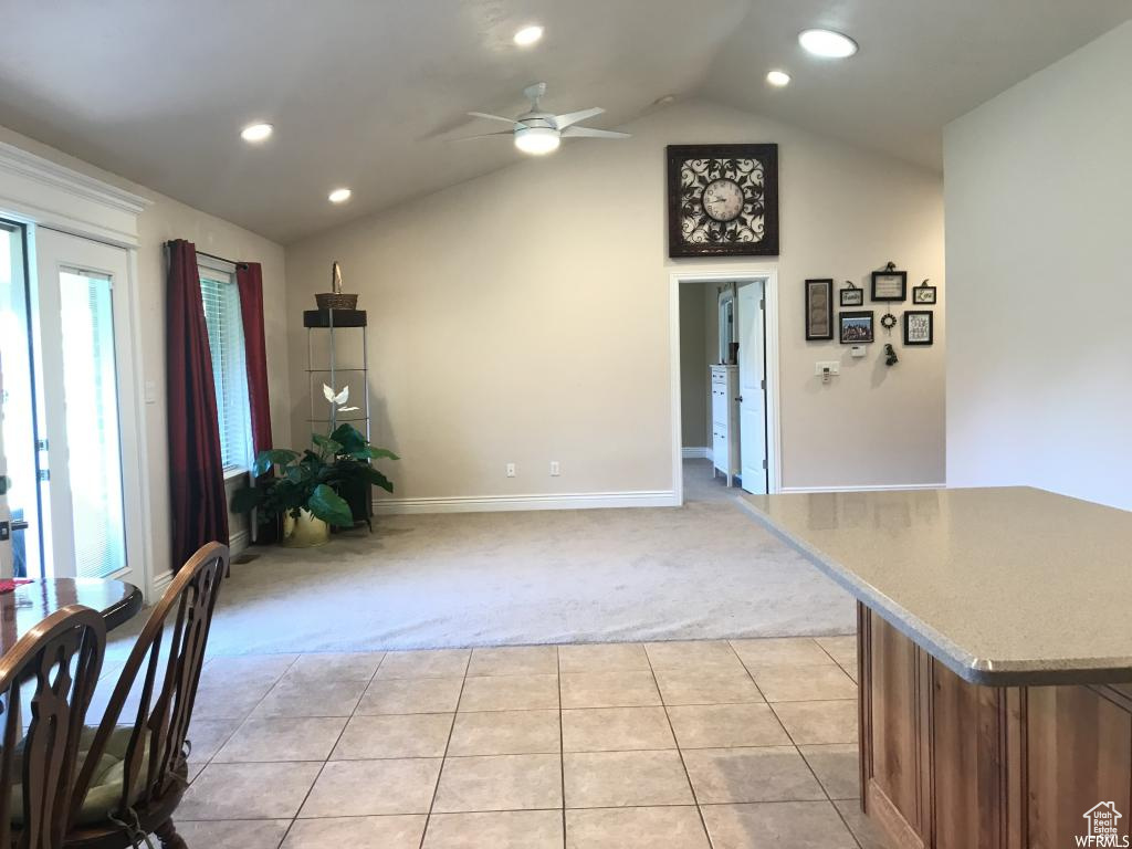 Unfurnished dining area with lofted ceiling, light carpet, baseboards, a ceiling fan, and light tile patterned floors