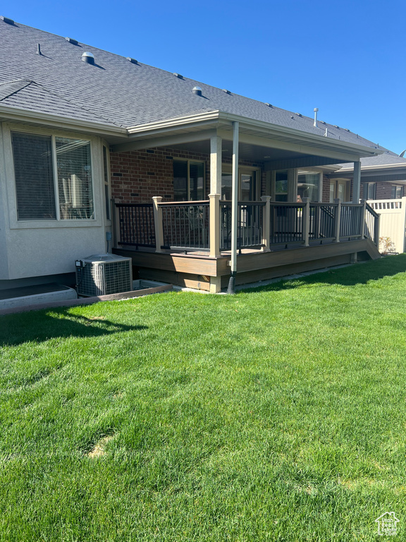 Rear view of house featuring roof with shingles, a lawn, a wooden deck, brick siding, and cooling unit
