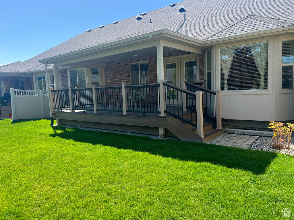 Back of property with brick siding, roof with shingles, a yard, and a deck