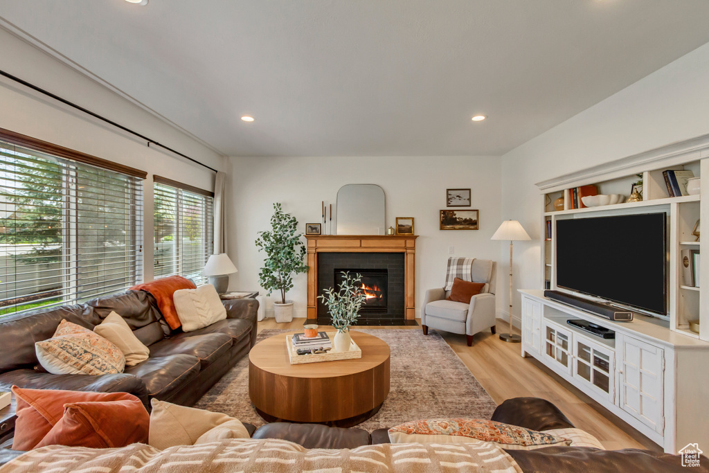 Living room featuring recessed lighting, a warm lit fireplace, and light wood finished floors