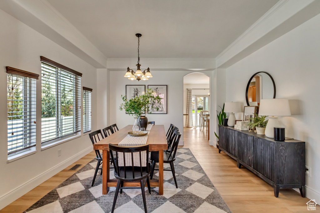 Dining area with arched walkways, a notable chandelier, light wood-style flooring, and a healthy amount of sunlight
