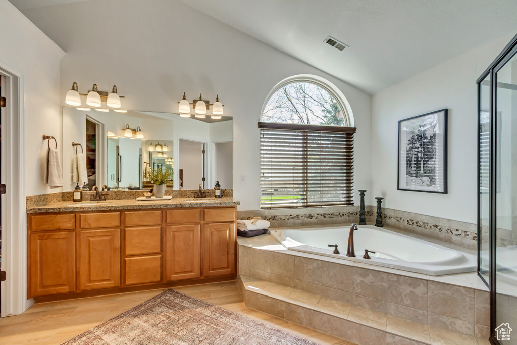 Bathroom with visible vents, a bath, lofted ceiling, and a sink