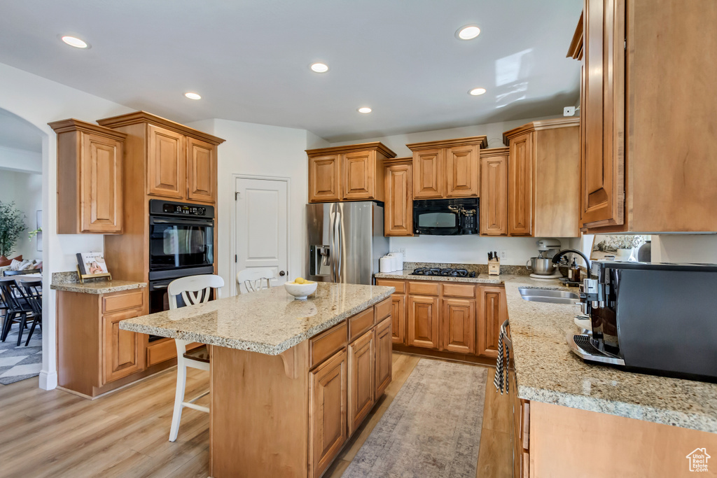 Kitchen with a breakfast bar, light wood-type flooring, black appliances, and a sink