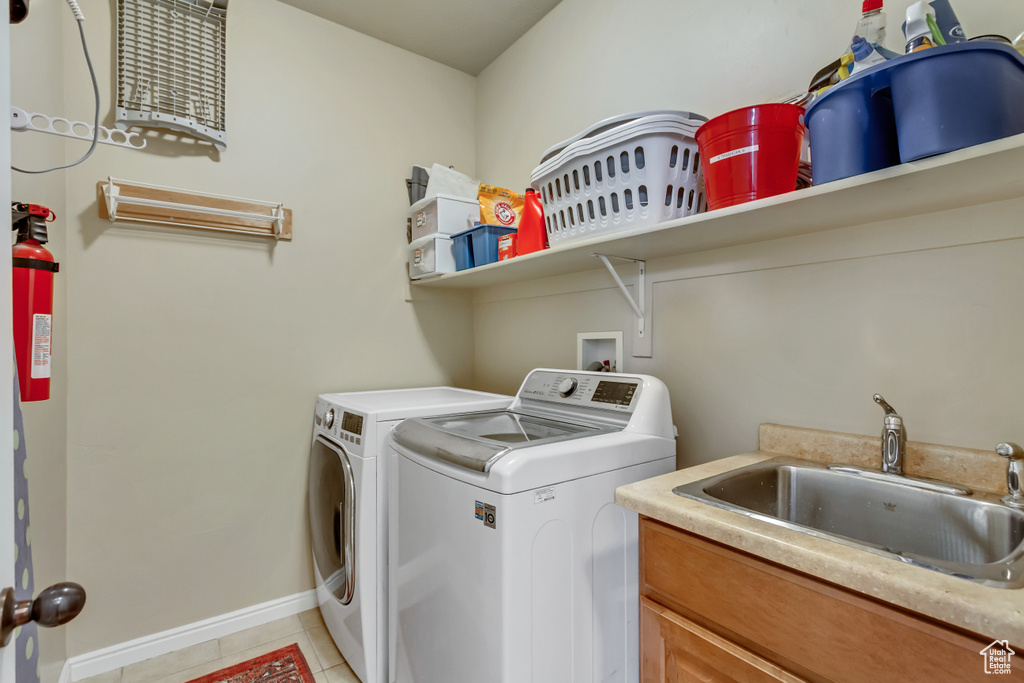 Washroom featuring light tile patterned floors, independent washer and dryer, a sink, baseboards, and cabinet space