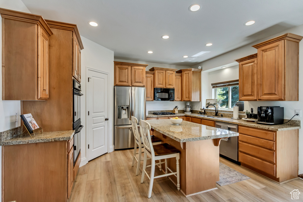 Kitchen featuring light stone countertops, a breakfast bar, black appliances, a sink, and a center island