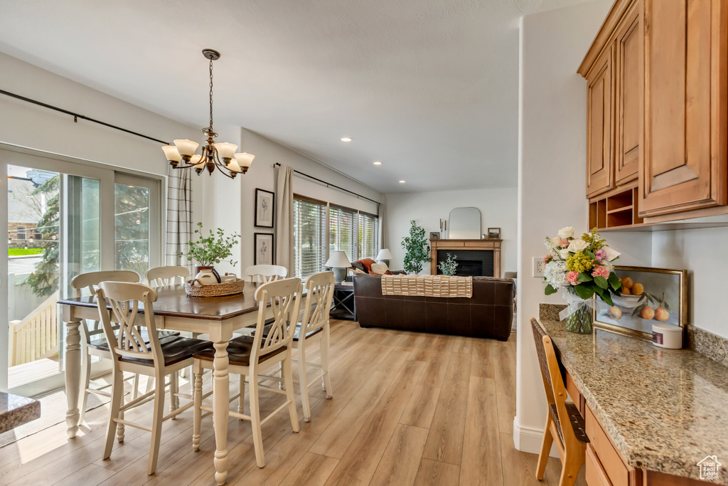 Dining space featuring a fireplace, light wood-style floors, recessed lighting, and a notable chandelier