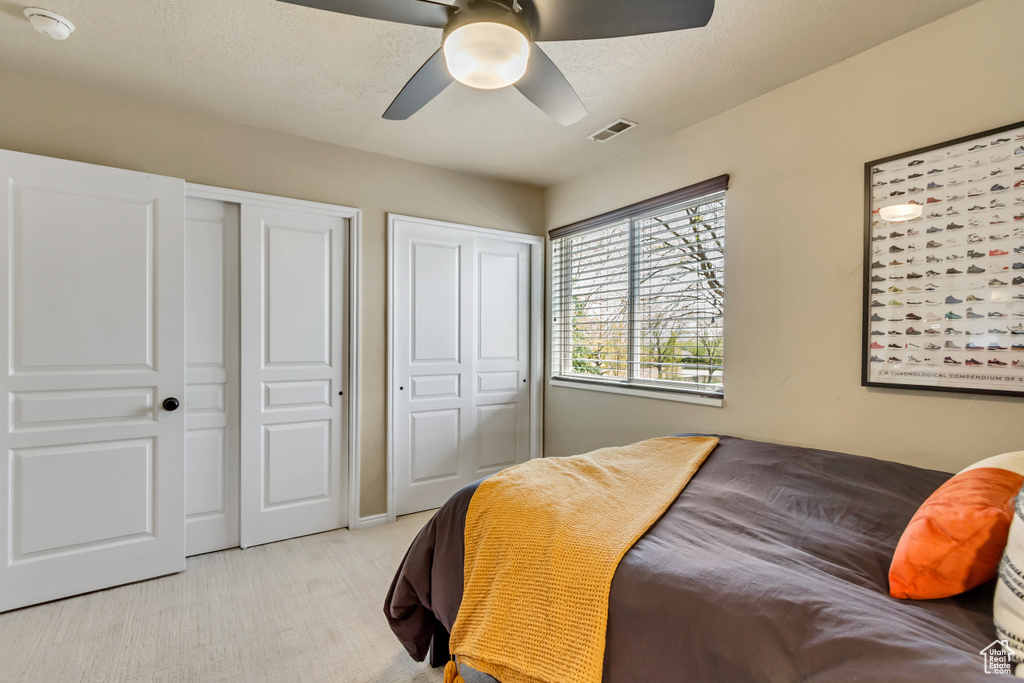 Bedroom with visible vents, a ceiling fan, light colored carpet, and two closets