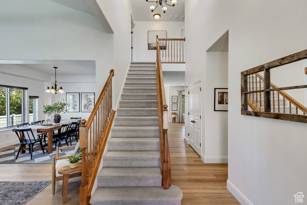 Staircase featuring a towering ceiling, a notable chandelier, wood finished floors, and baseboards