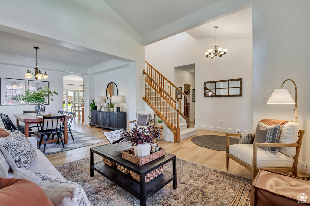 Living room featuring arched walkways, an inviting chandelier, wood finished floors, high vaulted ceiling, and stairs