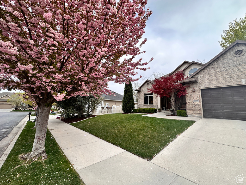 View of front facade featuring driveway, a front yard, an attached garage, fence, and brick siding
