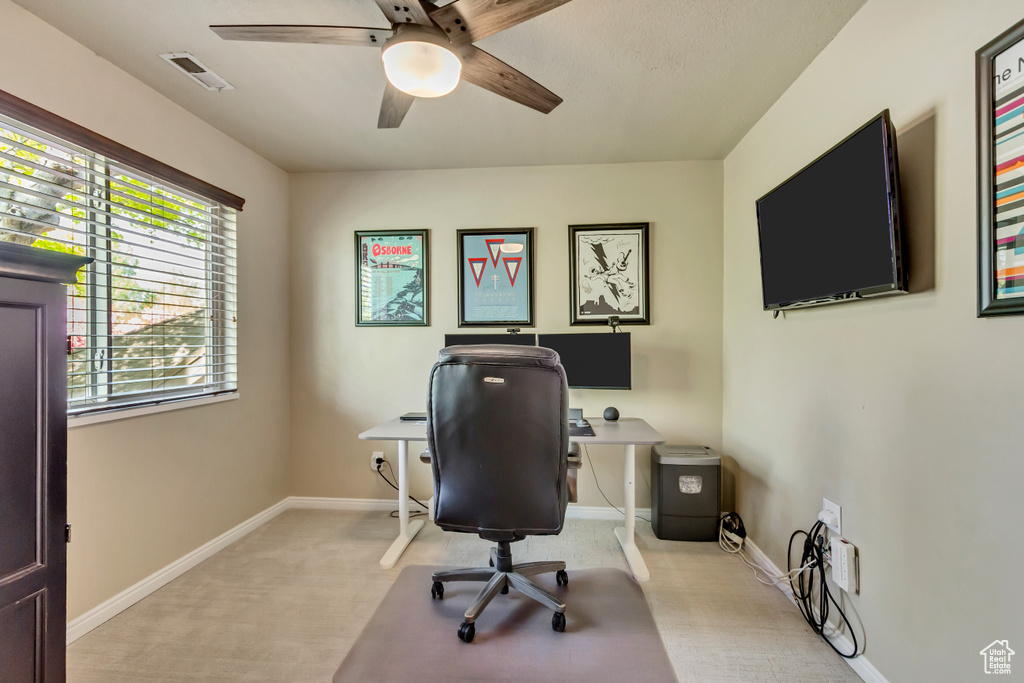 Home office with a ceiling fan, visible vents, light colored carpet, and baseboards