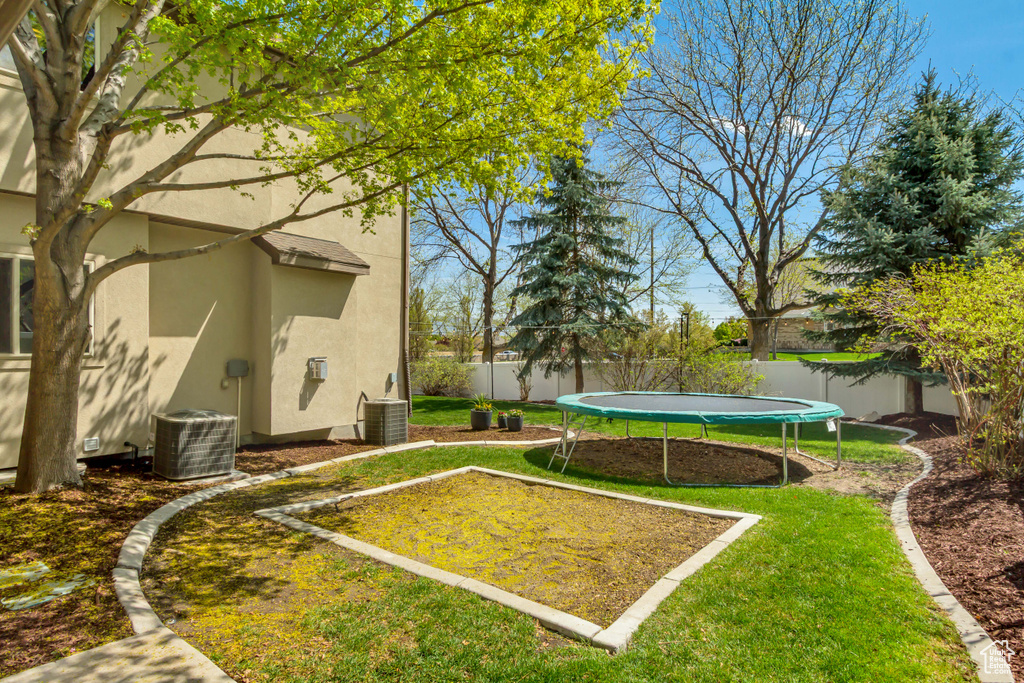View of yard featuring a trampoline, a fenced backyard, and cooling unit