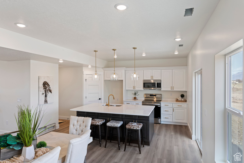 Kitchen featuring a kitchen breakfast bar, light wood-type flooring, white cabinetry, a sink, and stainless steel appliances