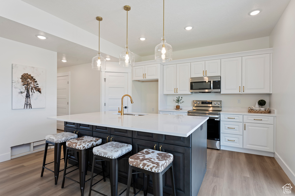 Kitchen with white cabinets, stainless steel appliances, a sink, and light wood-type flooring