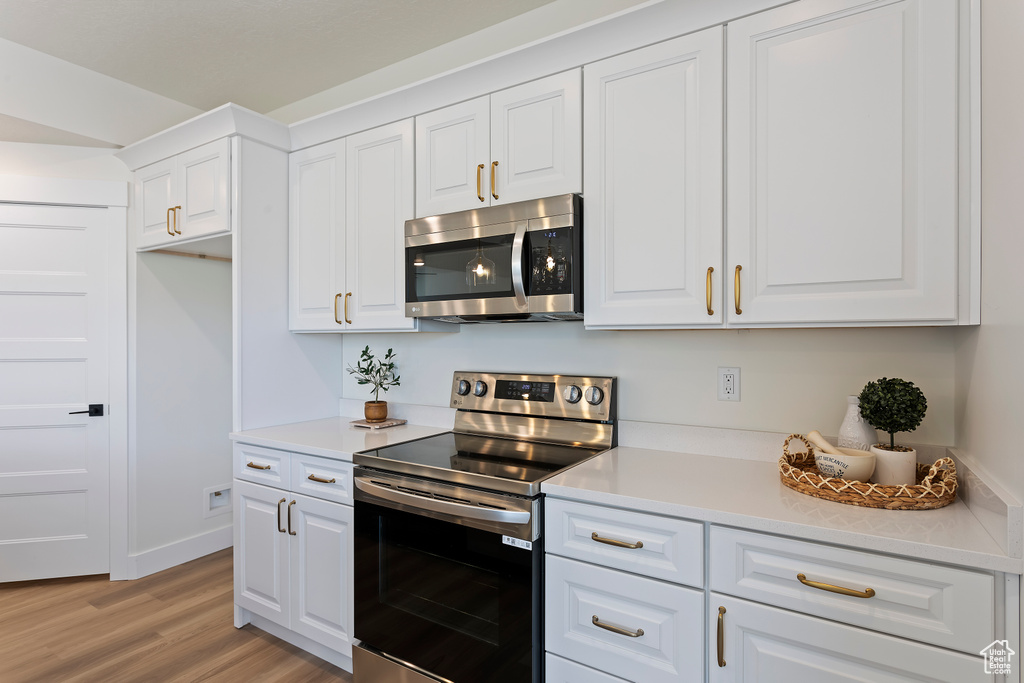 Kitchen with light countertops, appliances with stainless steel finishes, white cabinets, and light wood-type flooring