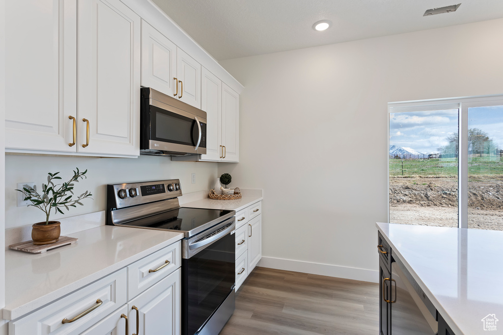 Kitchen with appliances with stainless steel finishes, light countertops, white cabinetry, baseboards, and light wood-type flooring