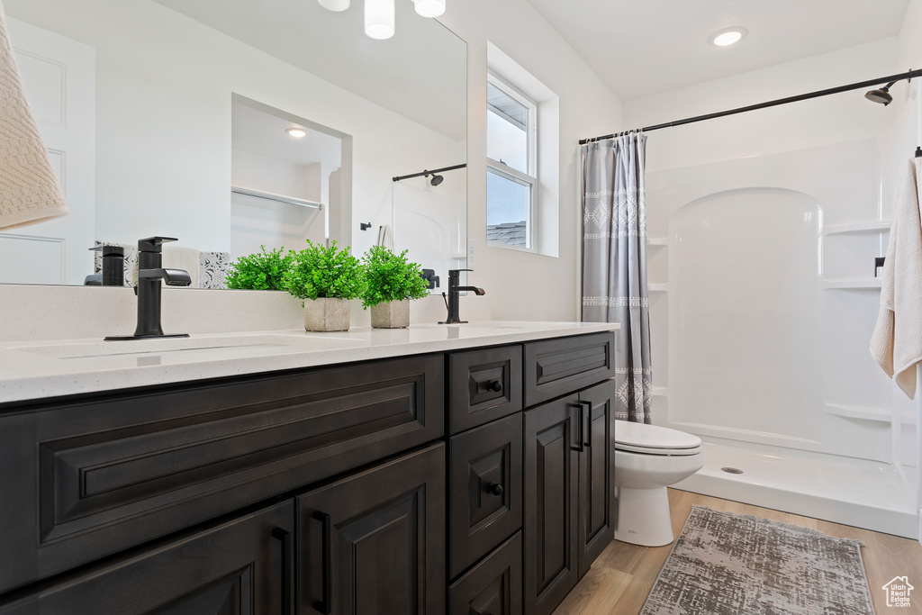 Bathroom with a sink, double vanity, toilet, wood finished floors, and a stall shower