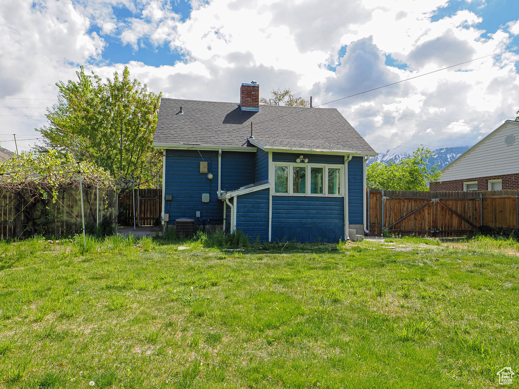 Back of property with a fenced backyard, a chimney, a yard, and roof with shingles