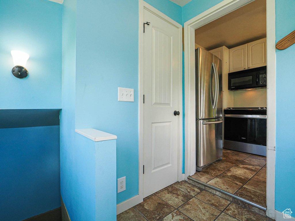 Kitchen with stone finish floor, range, black microwave, baseboards, and freestanding refrigerator