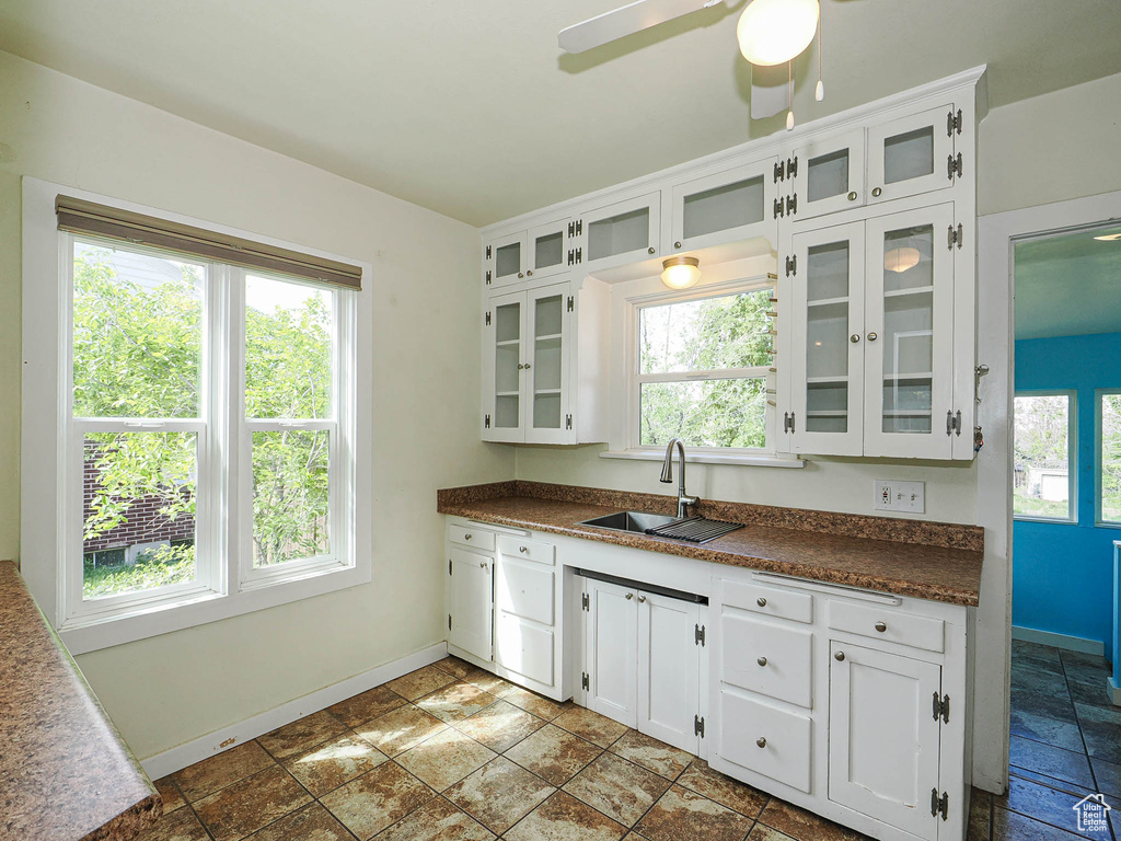 Kitchen featuring a sink, baseboards, dark countertops, and white cabinetry
