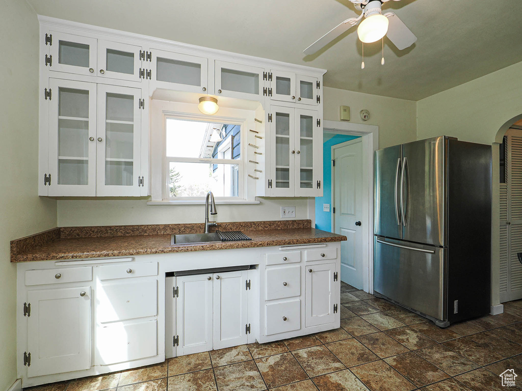 Kitchen featuring freestanding refrigerator, a ceiling fan, dark countertops, white cabinets, and a sink