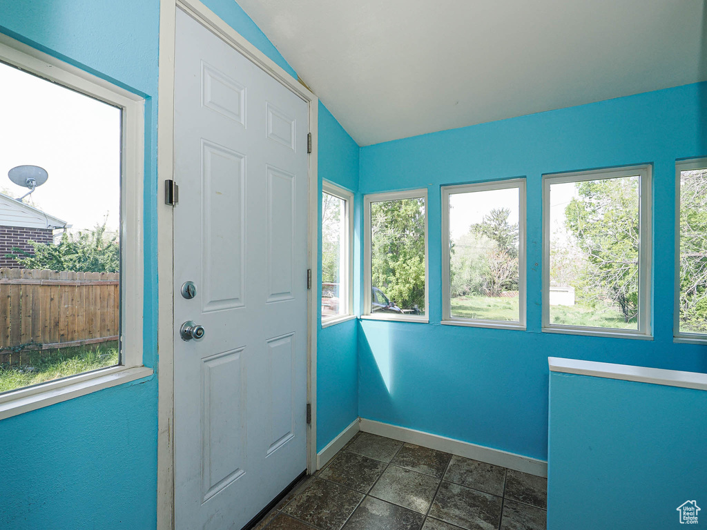 Entryway with baseboards, plenty of natural light, vaulted ceiling, and stone tile flooring