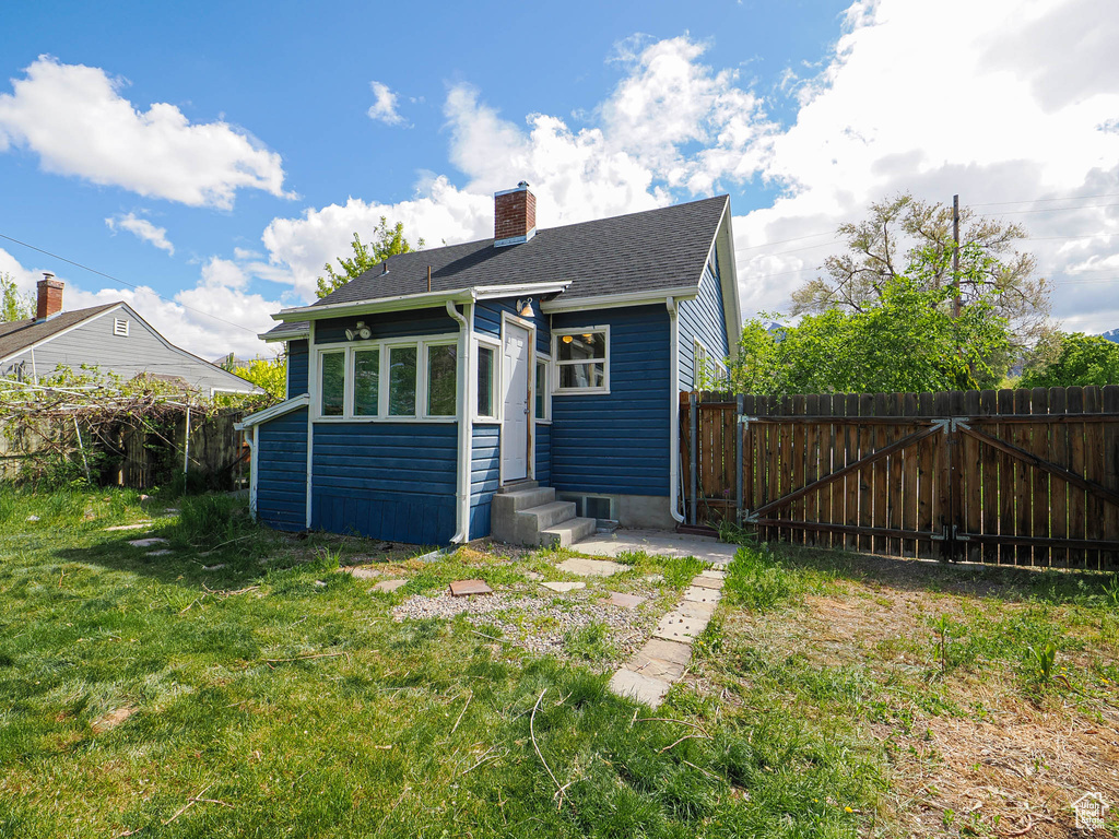Rear view of property featuring a chimney, a lawn, fence, a shingled roof, and entry steps