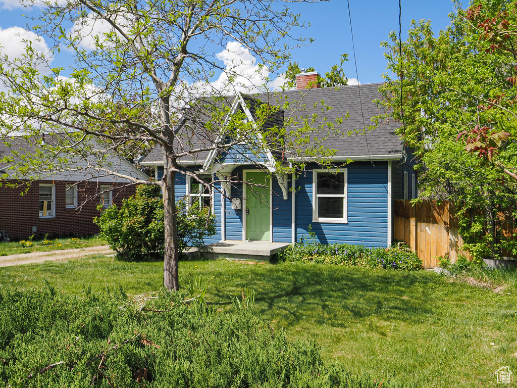 View of front facade with fence, a shingled roof, a chimney, and a front yard