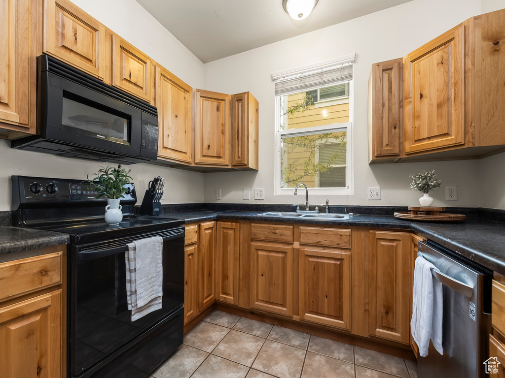 Kitchen featuring dark countertops, brown cabinets, a sink, light tile patterned floors, and black appliances