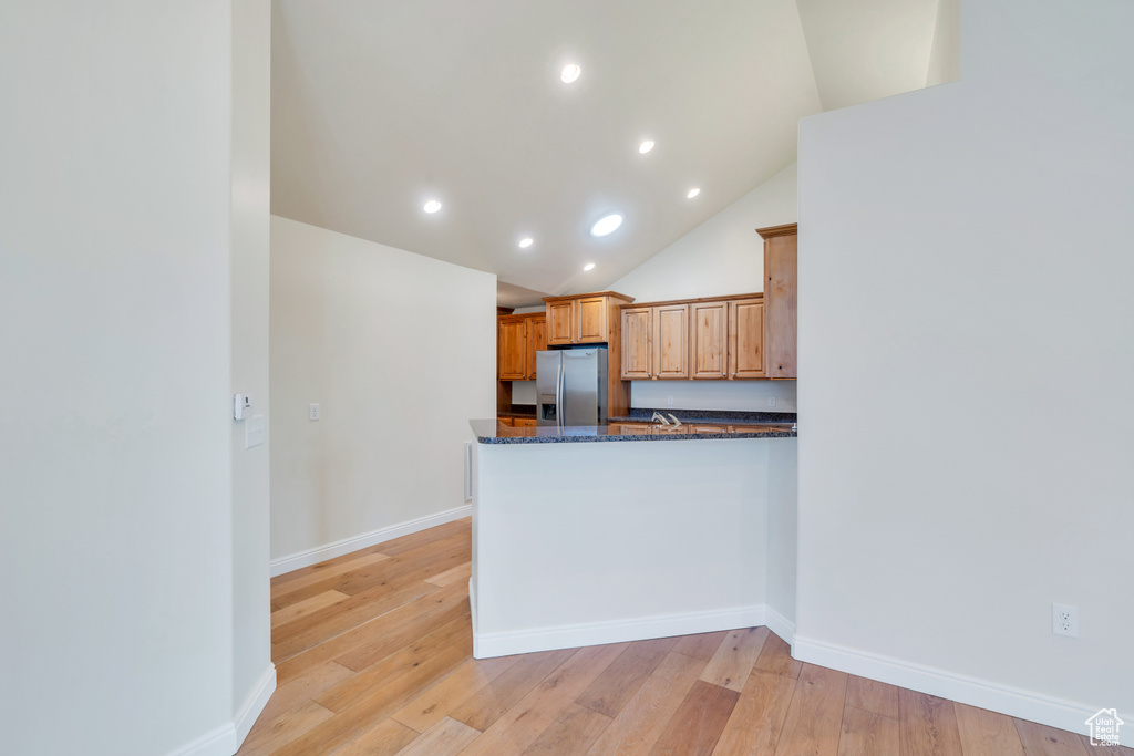 Kitchen with dark stone counters, recessed lighting, light wood-style flooring, and stainless steel fridge with ice dispenser