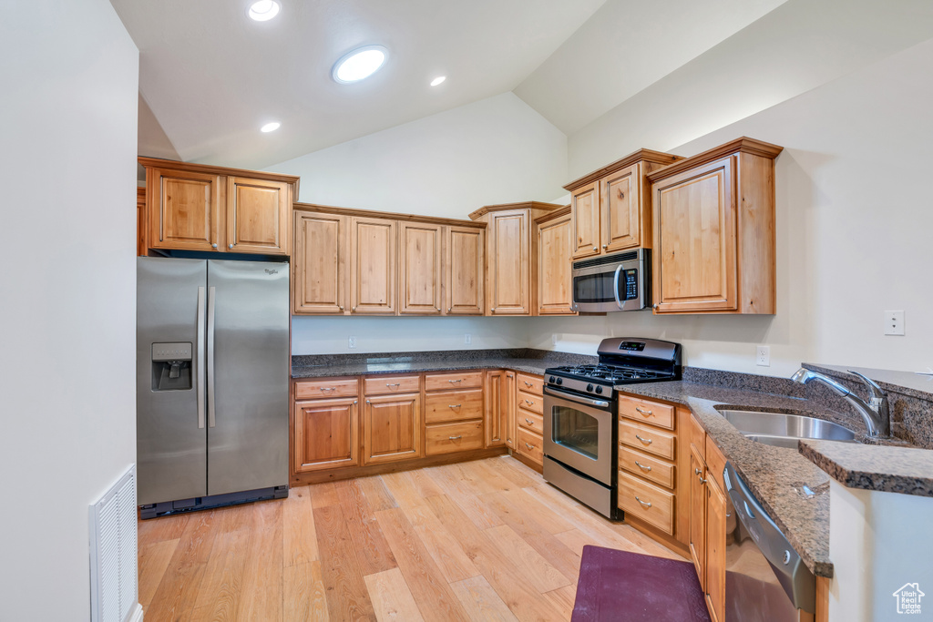 Kitchen featuring visible vents, appliances with stainless steel finishes, light wood-type flooring, a sink, and dark stone countertops