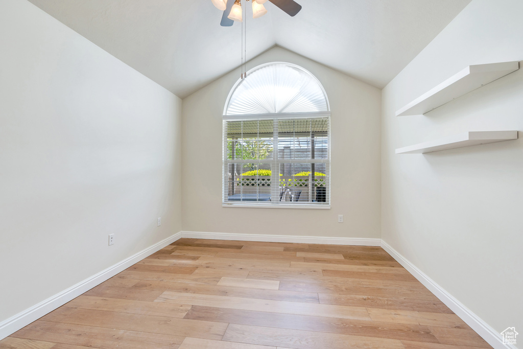 Empty room featuring a ceiling fan, baseboards, lofted ceiling, and light wood-style floors
