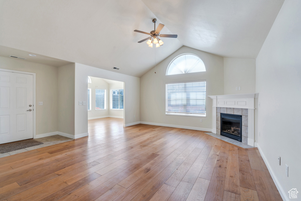 Unfurnished living room featuring ceiling fan, visible vents, a fireplace, vaulted ceiling, and light wood-style flooring
