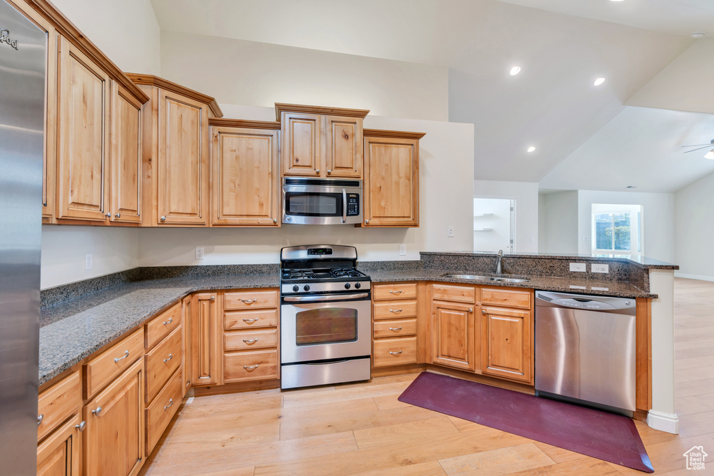 Kitchen with a sink, light wood-style floors, stainless steel appliances, a peninsula, and vaulted ceiling