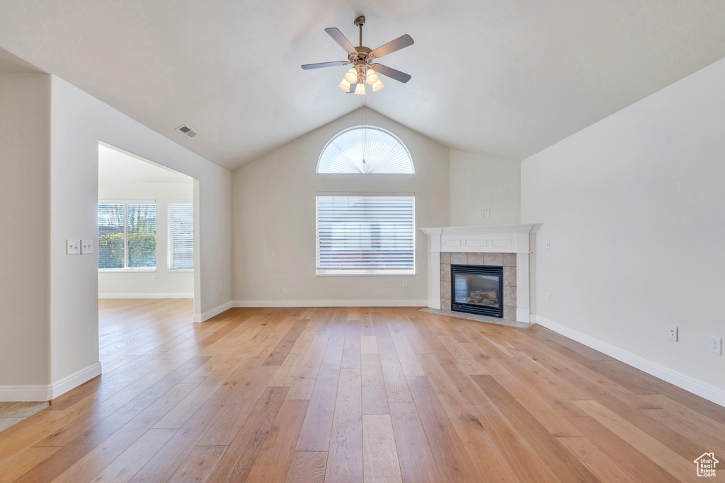 Unfurnished living room with a tiled fireplace, vaulted ceiling, light wood-style flooring, and visible vents
