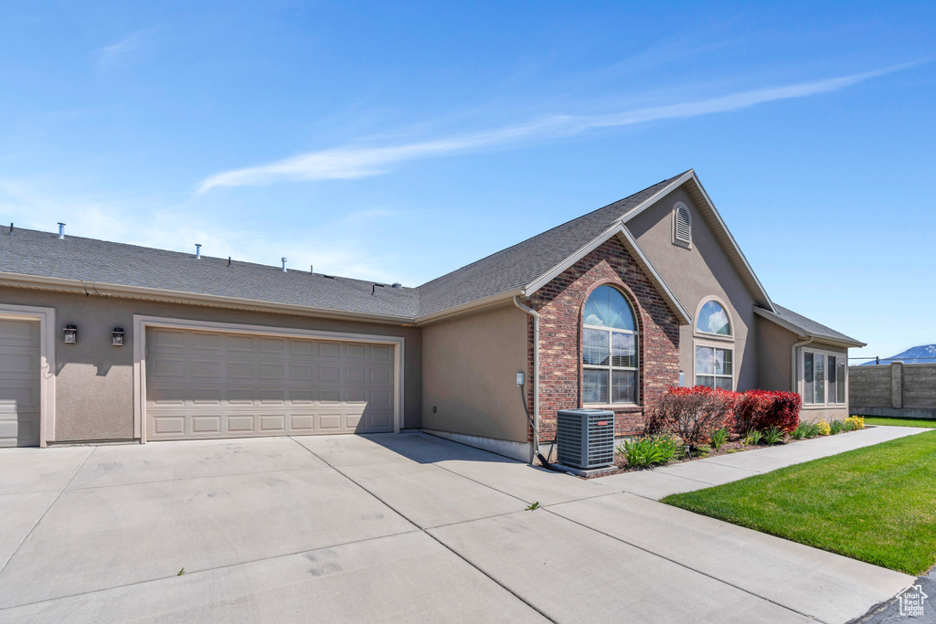 Ranch-style home with driveway, a garage, central AC, fence, and stucco siding