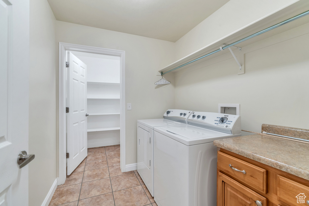 Clothes washing area with washing machine and clothes dryer, light tile patterned flooring, and baseboards