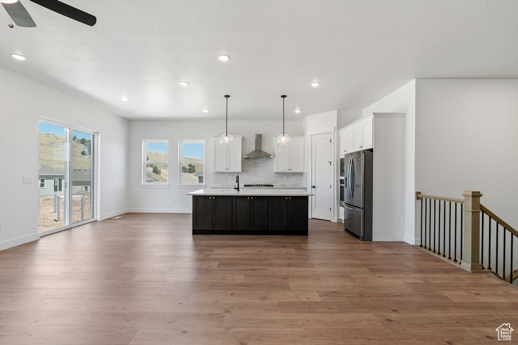 Kitchen with wall chimney range hood, stainless steel fridge, light countertops, a ceiling fan, and open floor plan