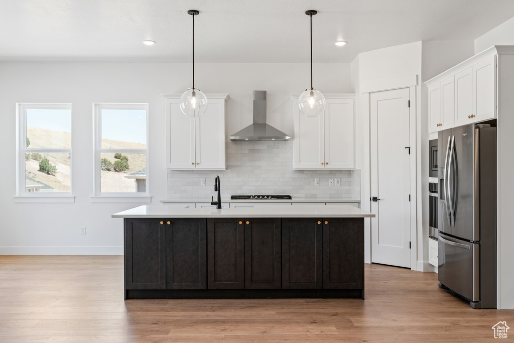Kitchen featuring wall chimney range hood, stainless steel refrigerator with ice dispenser, white cabinetry, and light countertops